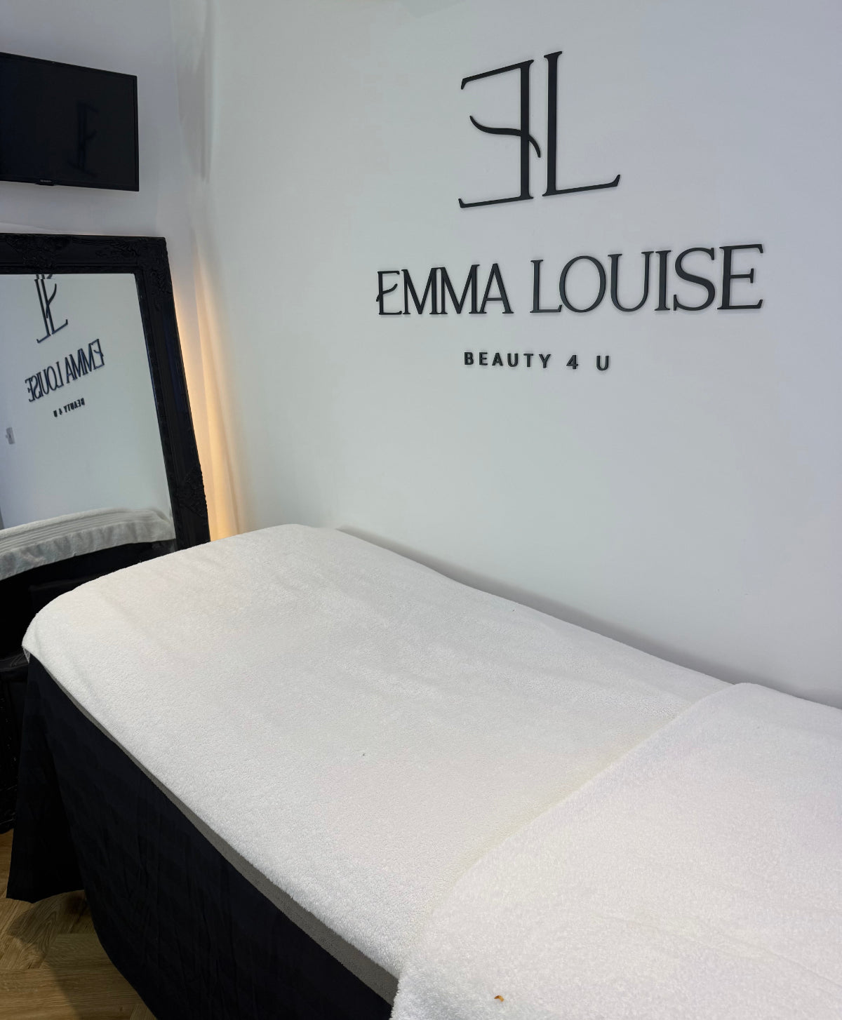 Treatment bed in a spa setting with 'Emma Louise Beauty 4 U' branding on the wall.